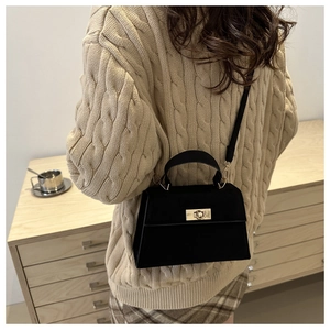 Detail of a black suede trapezoid handbag with a golden twist lock and adjustable strap