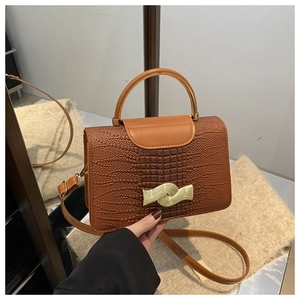 Detail of crocodile embossed brown leather bag with golden semi-circular metal handle