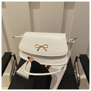 Close-up of white leather crossbody bag featuring a decorative gold bow metal buckle