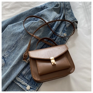 Detailed view of brown faux leather messenger bag with golden metal buckle on denim jacket