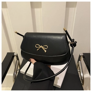 Close-up of a black crossbody bag with a decorative gold bow buckle and knotted strap