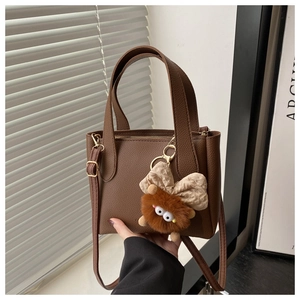 Detail of dark brown pebble leather bucket bag with cute monster plush charm and strap