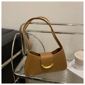 Detail of a brown leather shoulder bag with a gold crescent buckle on a minimal metal shelf