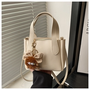 Detail of off-white lychee pattern leather bucket bag with a cute brown plush pendant