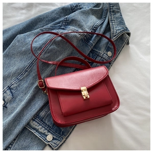 Detail of red messenger bag with flap closure and golden metal buckle on denim jacket