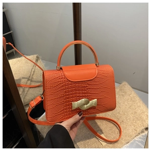 Detail of orange crocodile pattern leather bag with wave-shaped gold metal lock and handle