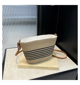 Détail d'un sac seau en paille avec rayures noires et bandoulière en cuir marron