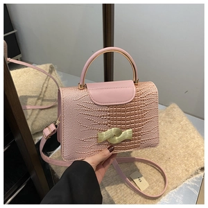 Detailed view of pink crocodile texture with wavy gold buckle and metal top handle
