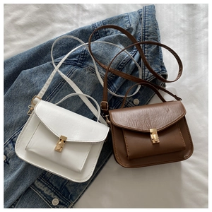 Detail of white and brown messenger bags with golden metal push-locks on denim background