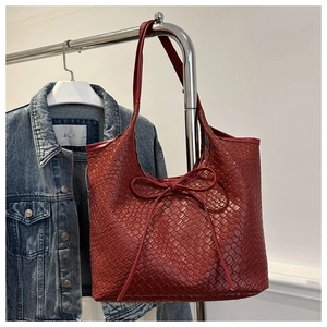 Detail of red woven faux leather tote bag with elegant bow accent on denim jacket