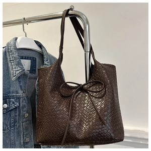 Detail of dark brown woven tote bag featuring an intricate pattern and a decorative bow