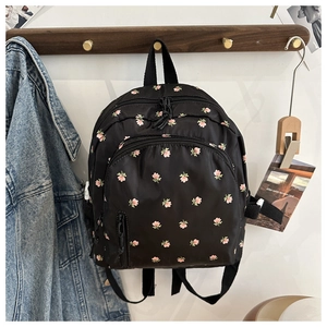 Detail of black nylon backpack with small floral patterns hanging on a wooden hook