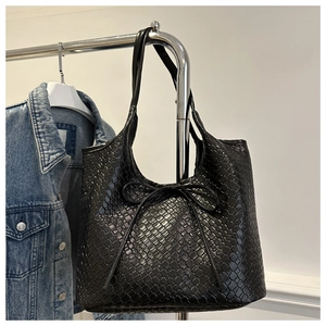 Detail of black woven leather tote bag featuring a decorative bow on the front surface