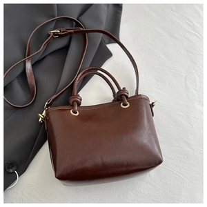 Detail of dark brown PU leather bucket bag with knotted handles and golden hardware
