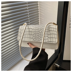 Close-up of a white shoulder bag with black crocodile pattern embossed on the flap