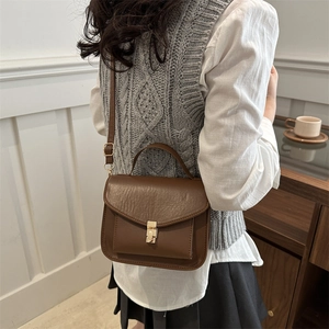 Vintage brown leather messenger bag with gold clasp shown on a model in a cafe setting