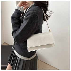 Close-up of white woven textured flap handbag with gold metal hardware on model