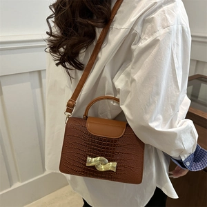 Brown crocodile embossed leather crossbody bag with wave gold buckle worn on white shirt