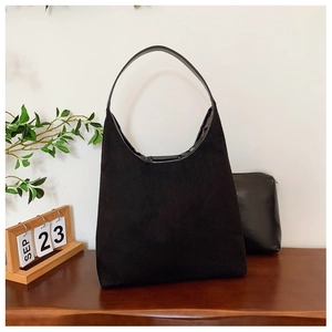 Detail view of black matte leather tote bag and inner pouch on a dark wooden table