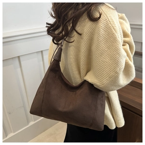 Model wearing a dark brown suede hobo bag with leather strap in a bright minimalist room