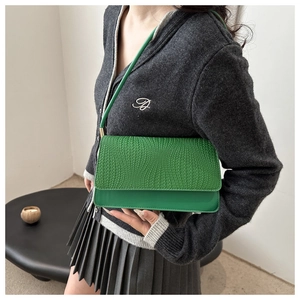 Detail of green shoulder bag featuring a woven texture flap and smooth finish leather