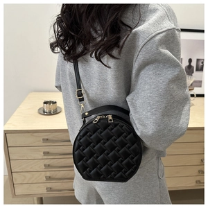Detail of a black quilted round crossbody bag with gold zippers worn by a model