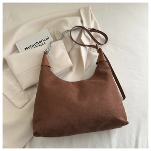 Detail of a brown suede hobo bag with a silver chain strap on a chic beige blazer