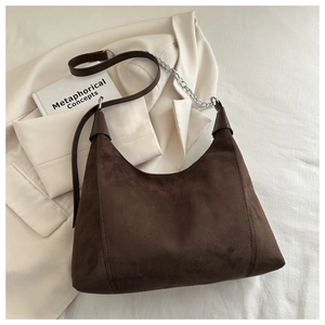 Detail of dark brown suede hobo bag with silver chain strap on beige blazer