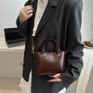 Minimalist dark brown leather bucket bag with top handles and a detachable shoulder strap