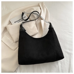 Detail of black suede hobo bag with silver chain strap on a white blazer background