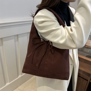 Retro dark brown suede tote bag with side bow detail worn by a model in a minimalist room