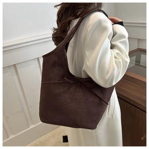 Détail du sac bandoulière en daim marron avec nœud porté sur un blazer blanc chic