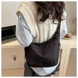 Model wearing a large black nylon crescent crossbody bag in a minimalist cafe setting
