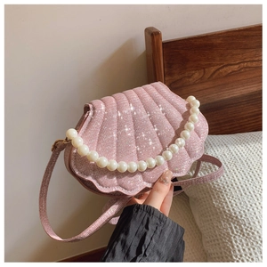 Detail of pink glitter shell bag featuring pearl handle and shiny sequin strap in hand