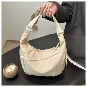 Close-up of cream nylon crescent shoulder bag with adjustable strap and functional zippers