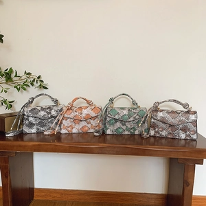 Fashionable snakeskin crossbody bags in four colors arranged on a wooden bench