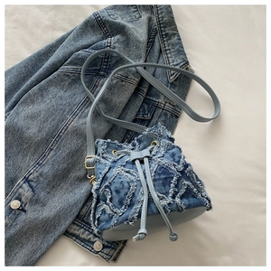 Detail of light blue denim bucket bag with frayed fringe texture and adjustable gold buckle