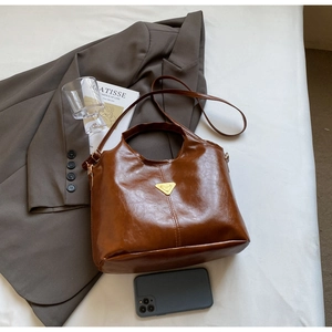 Deep brown faux leather tote bag with metal triangle logo on a white bed sheet