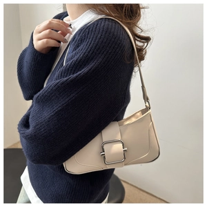 Sac baguette chic en cuir crème avec boucle argentée porté à l'épaule sur pull bleu
