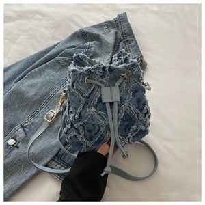 Detail of light blue denim bucket bag with frayed edges and drawstring closure