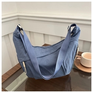 Detail of grey-blue nylon shoulder bag with zipper and wide strap on wooden table