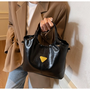 Detail of black glossy leather bucket bag with metallic triangle logo and rounded handles