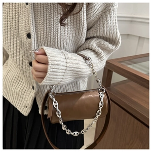 Détail d'un sac cylindrique marron avec chaîne argentée et bandoulière en cuir