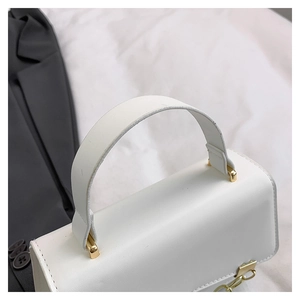 Detail of the white synthetic leather handle and gold chain hardware on a small square bag