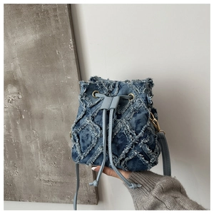 Close-up of quilted denim bucket bag with fringe details and leather drawstring hardware