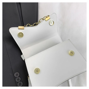 Detail view of white crossbody bag showing golden magnetic buckles and inner storage space
