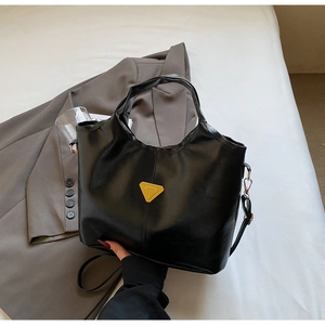 Macro detail of black glossy faux leather tote bag with gold triangle logo hardware