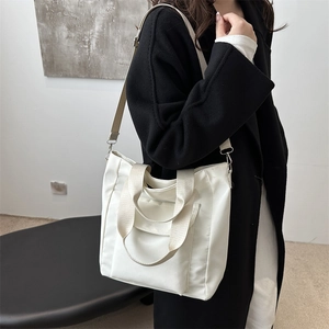 Minimalist white large capacity tote bag with wide strap worn with a black coat