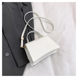 Top view of white trapezoid crossbody bag on grey blazer showing smooth leather texture