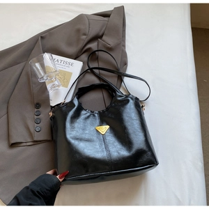 Detail view of a black glossy tote bag with golden triangle buckle on a white surface